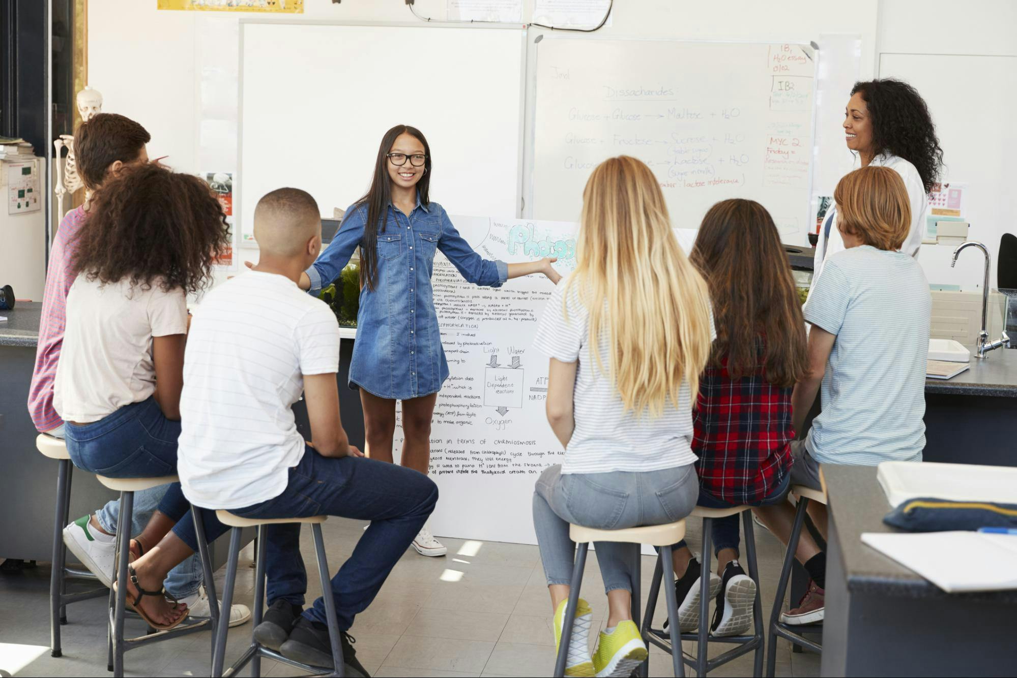 A high school student stands in front of her classmates and presents a project.