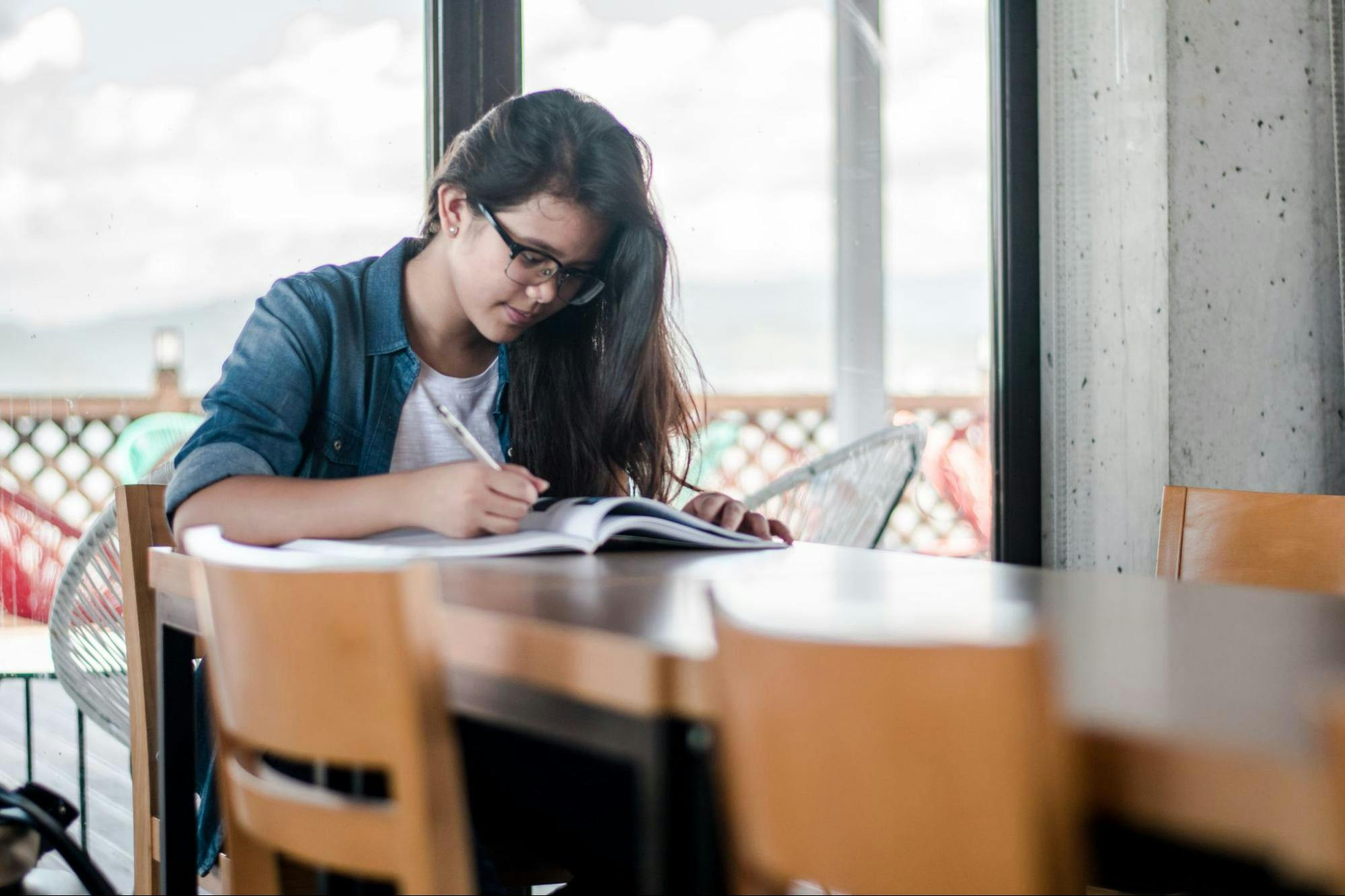 A female student sits alone at the end of a table and studies.