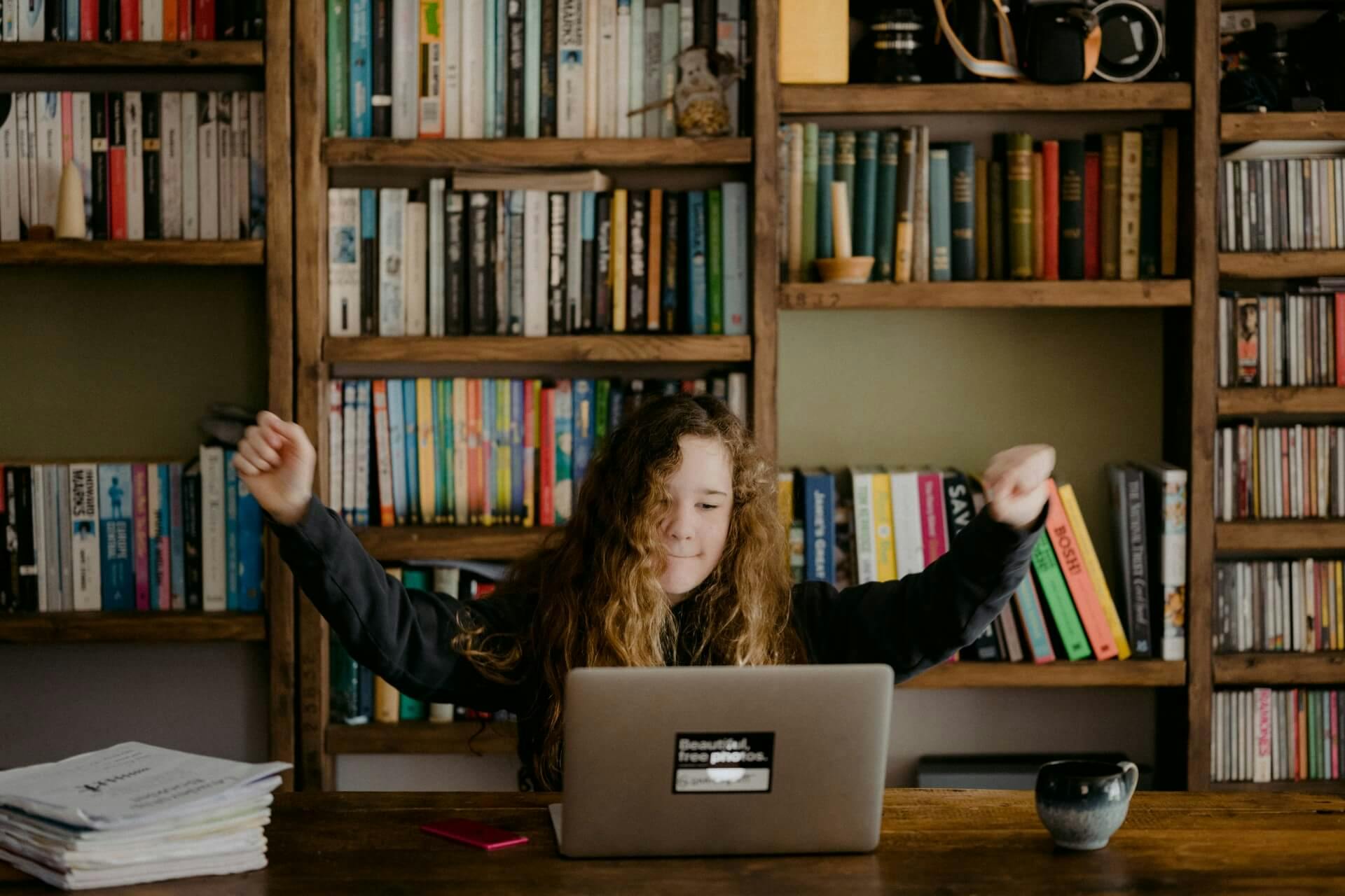 Student using laptop and raising arms in excitement.