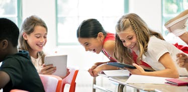 A group of elementary students laughing in class and using tablets.