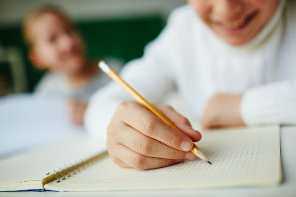 A student is drawing on a notebook, holding a pencil.