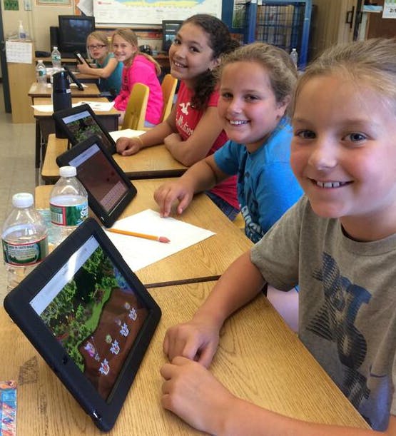 Five middle school students sitting at a row of desks playing Prodigy Math on tablets.