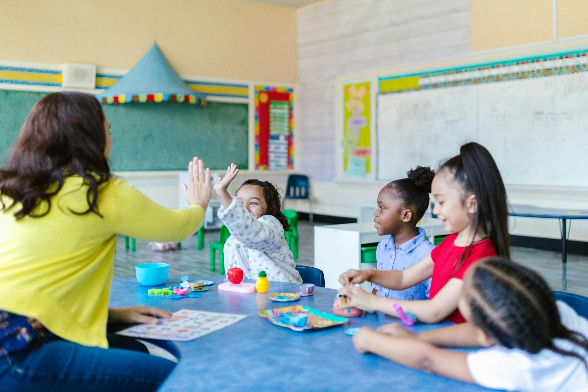 Four young students and a teacher sit at a table in a classroom in a positive learning environment.