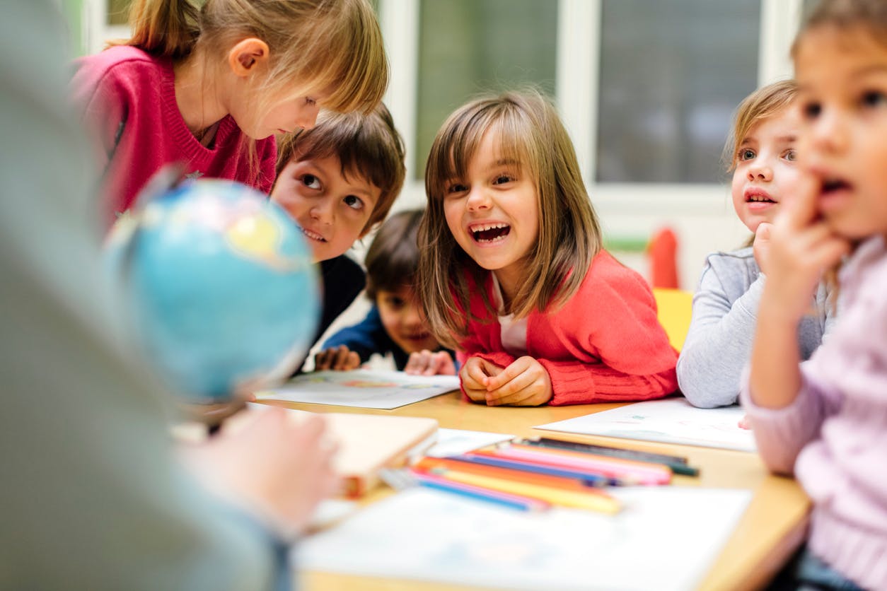 A group of primary students sitting and standing around a desk having an exciting conversation.