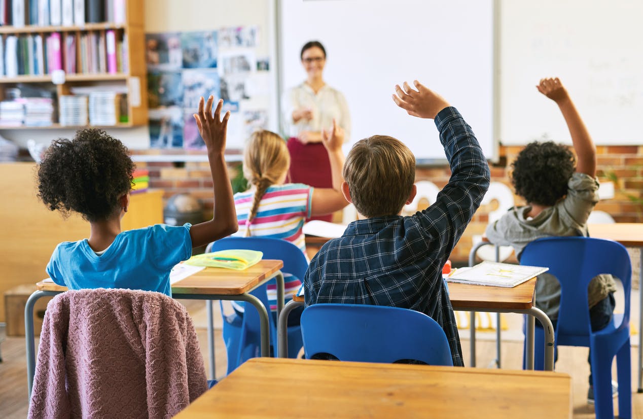 Four middle school students raising their hands to answer their teacher's question.