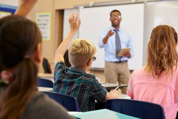 A teacher chooses from a group of students with their hands raised during a lesson.