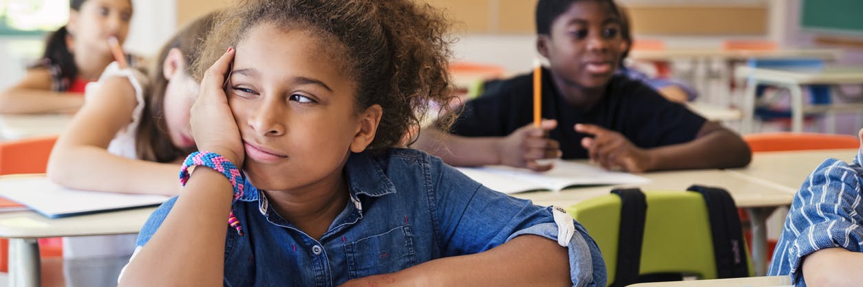 Child looking bored while sitting at her desk in school