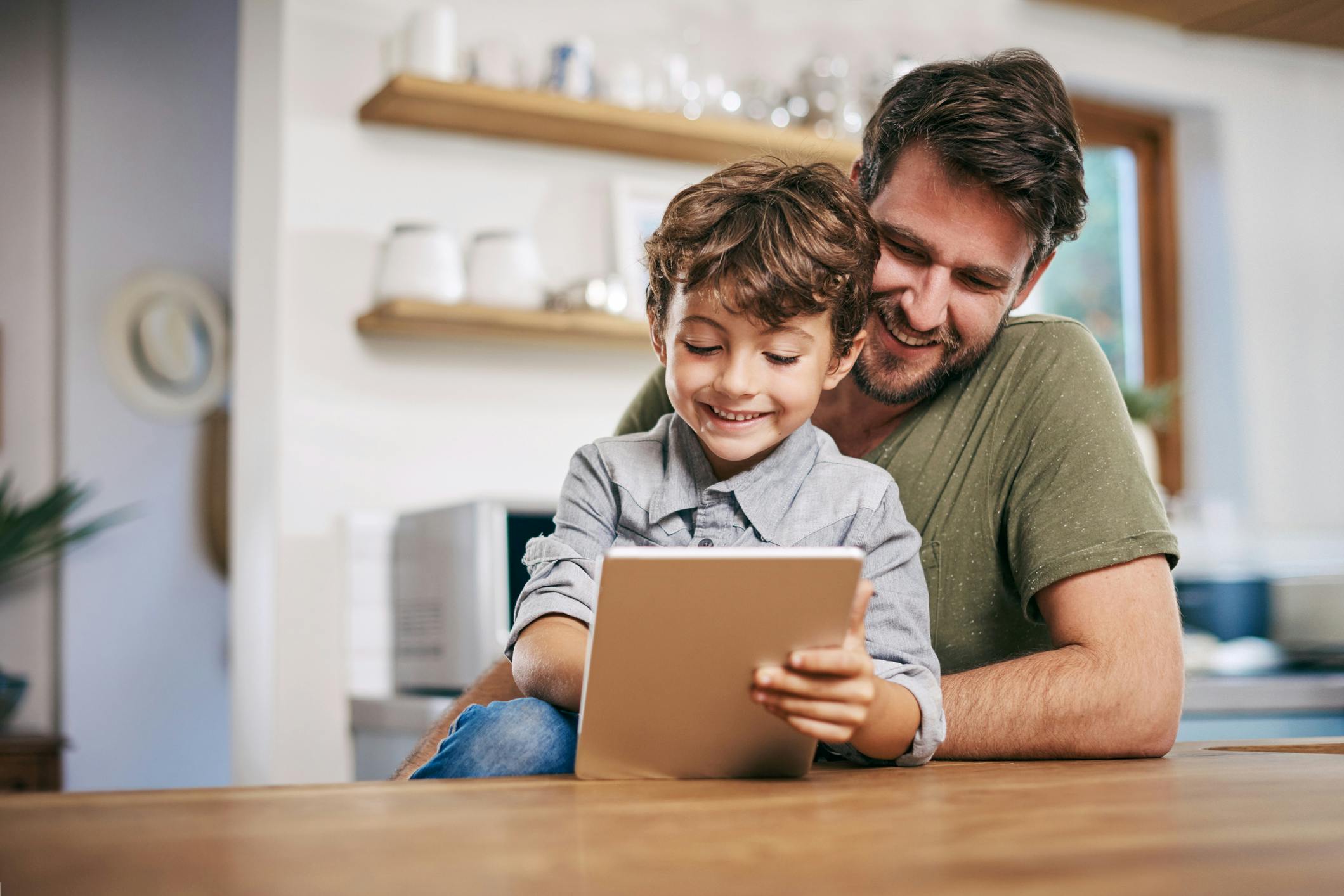 Happy child sitting with his father, playing Prodigy Math Game on a tablet to tackle boredom while learning