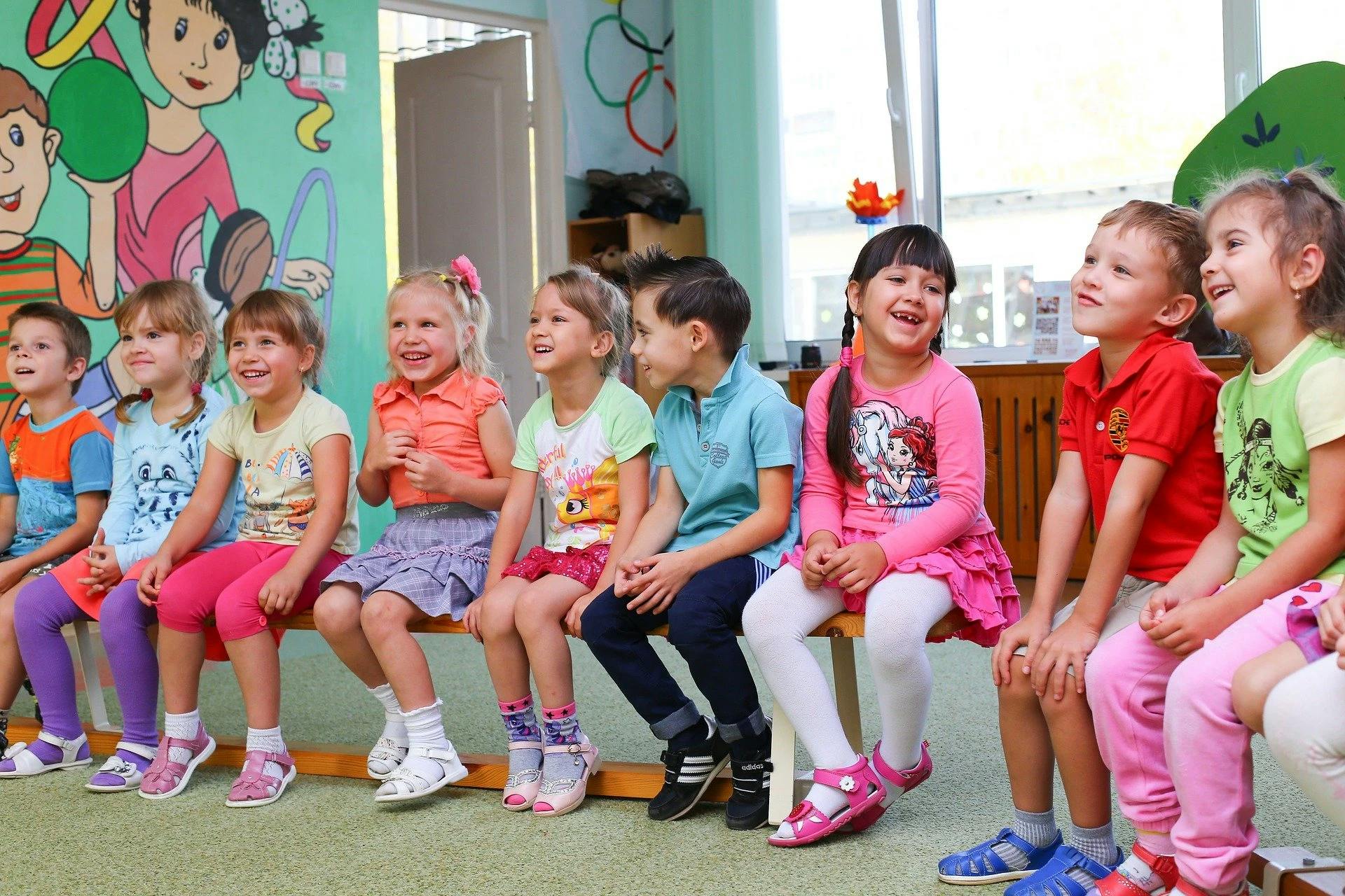 A class of young students sits in a row on benches and loots happy.