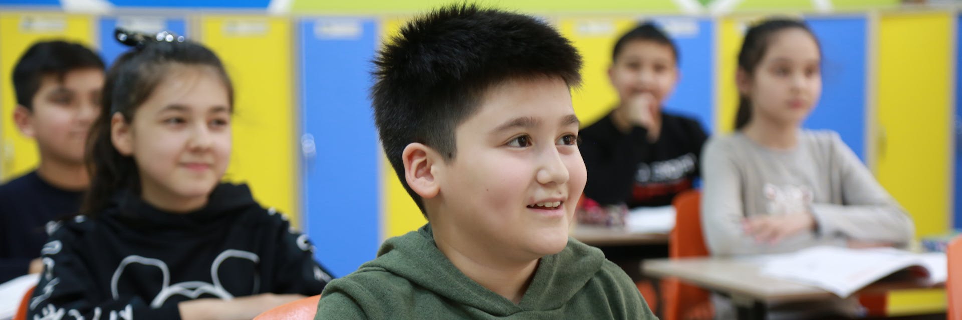 A group of five elementary students learning in class and smiling.