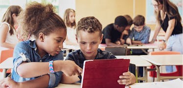 Two elementary students looking at a tablet in class.