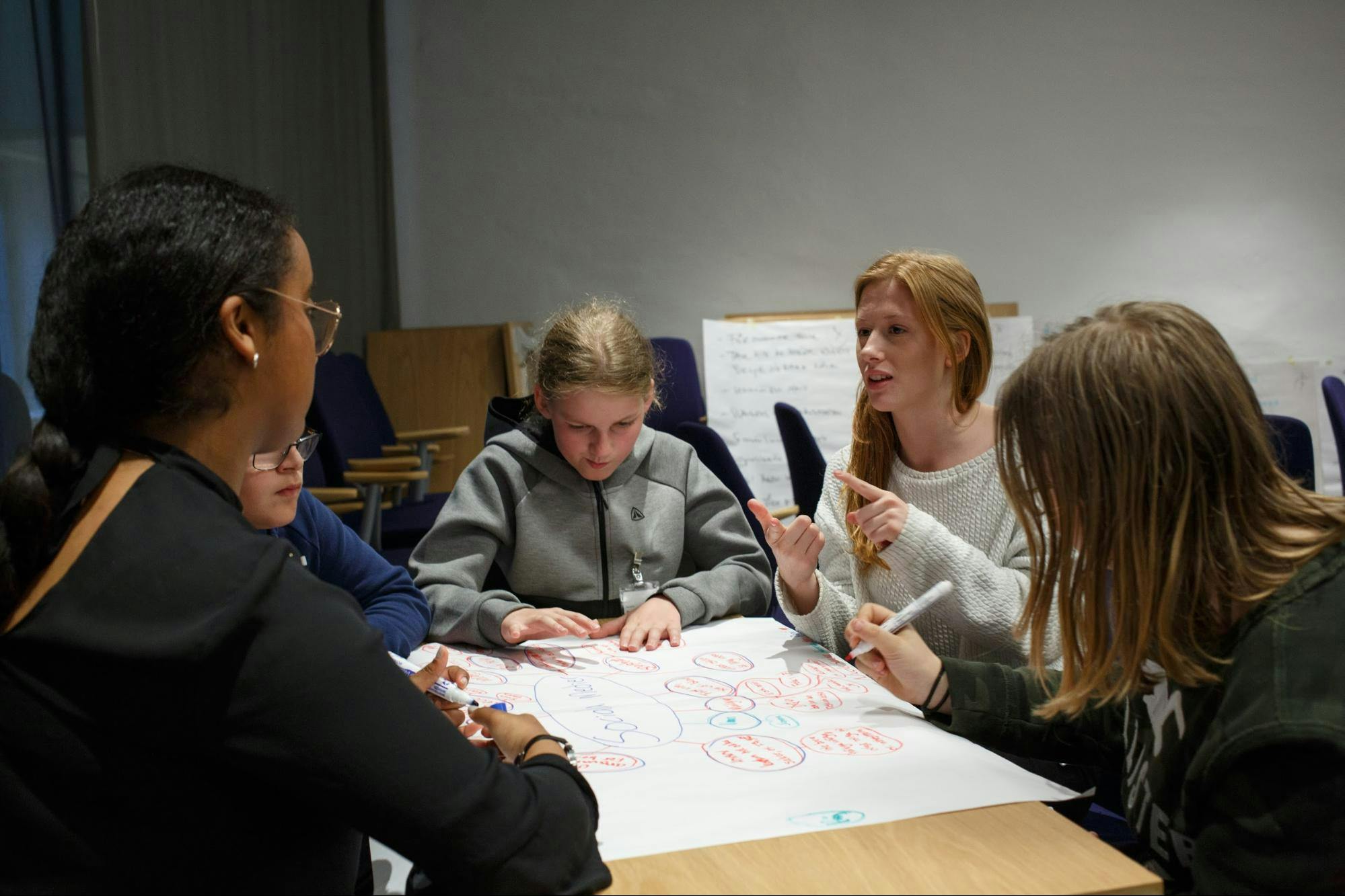 Five students sit around a table and discuss.