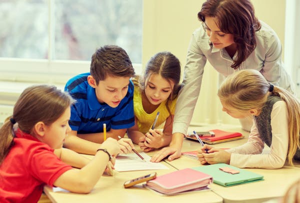 Teacher helping four students learn as they read through a shared worksheet.