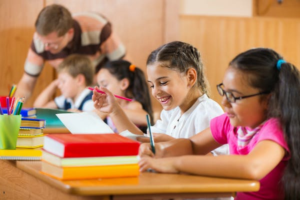 A happy student is doing her homework and a teacher is instructing others