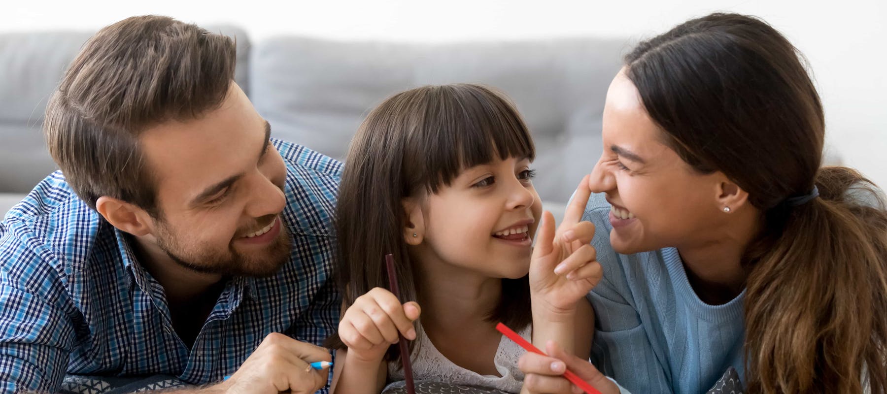 Child smiles and plays with her parents as they write in a journal together.