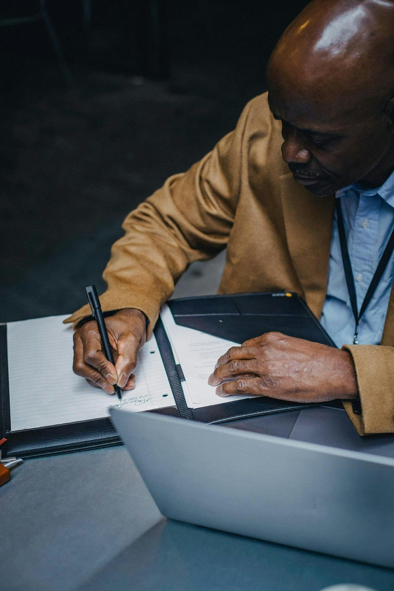 Man sits at desk and makes notes in a notebook in front of a computer.