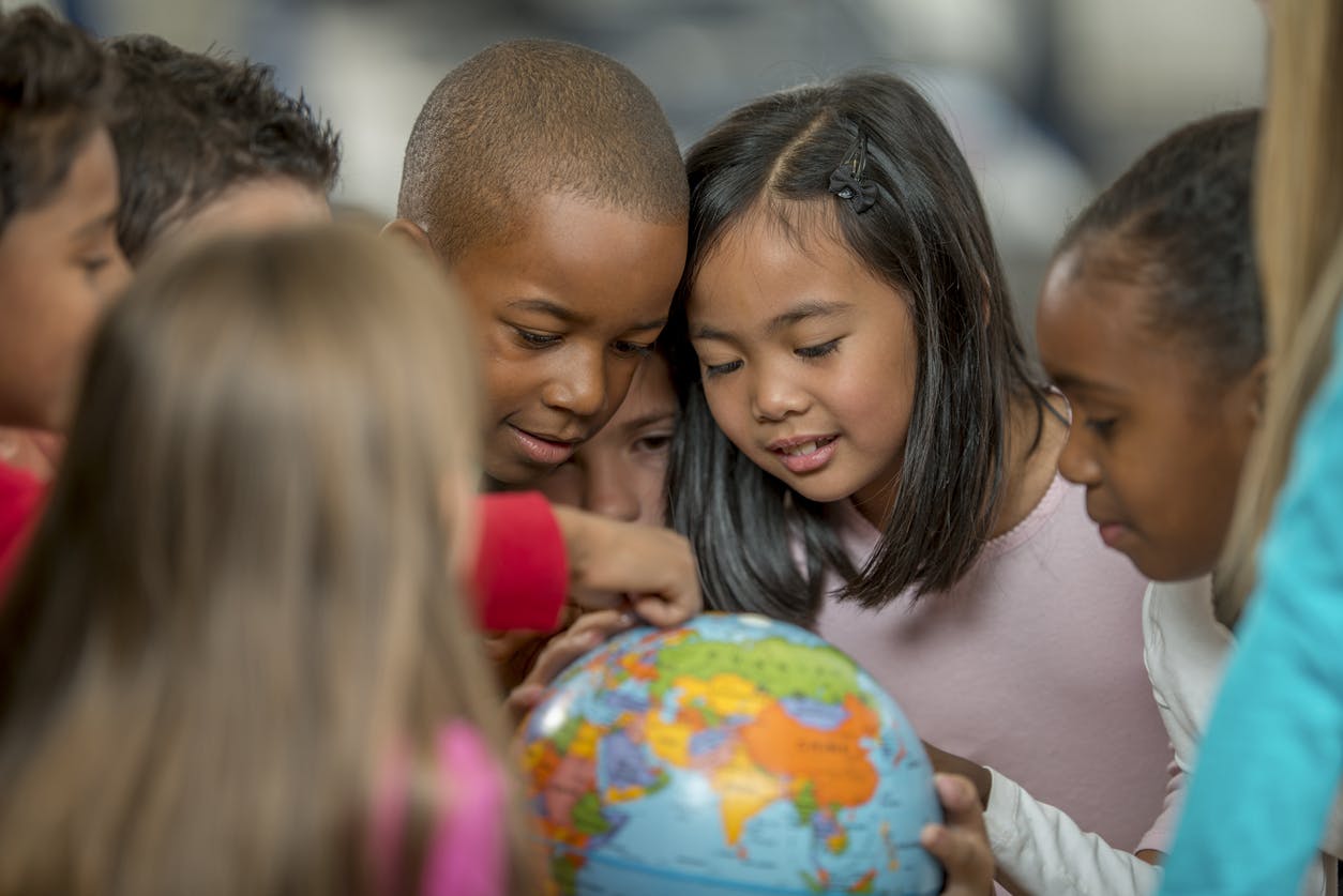 A diverse group of students gathering around a spinning globe in their classroom.