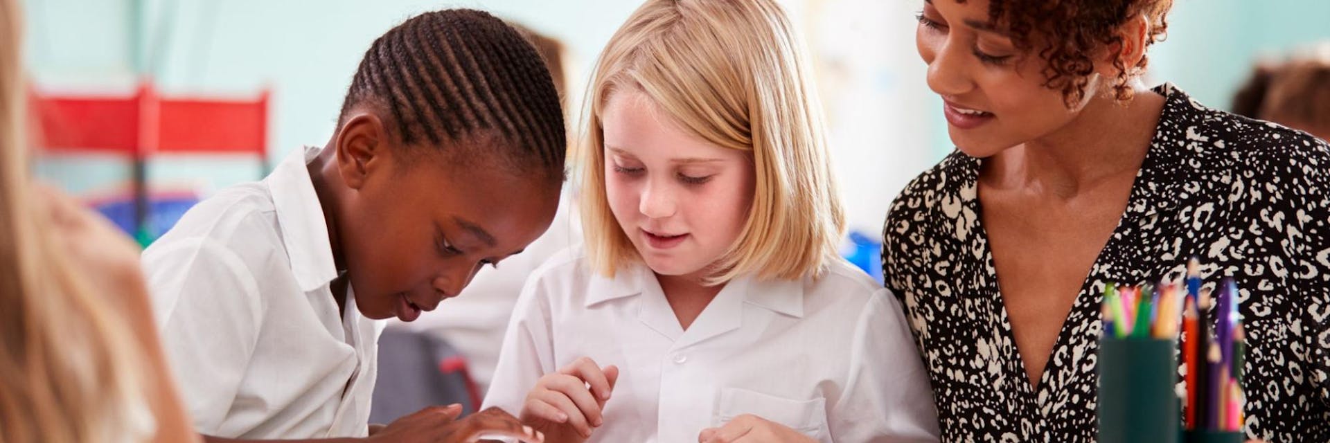 Two students and a teacher explore virtual field trips on a tablet in the classroom.