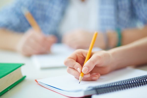 A child's hand holding a pencil and writing on a notebook.