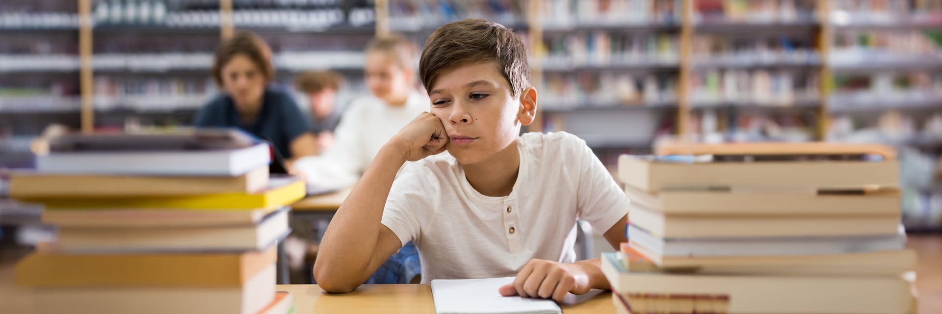 A boy studying at a desk in a library filled with books.