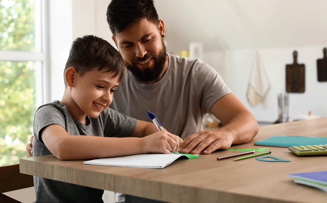  A dad and a son are at a table, both writing, highlighting a bonding moment